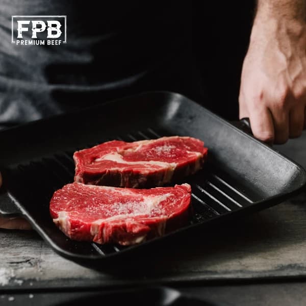 Two marbled grass-fed steaks searing in a cast-iron grill pan