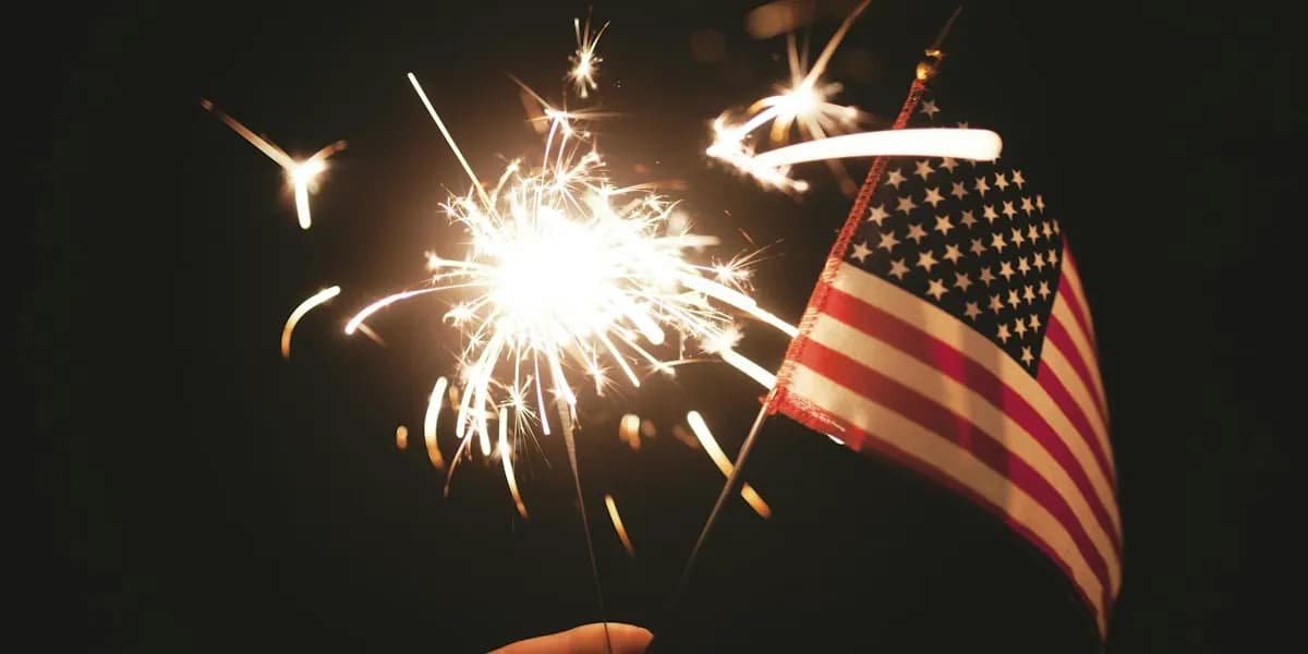 A lit sparkler next to a small American flag at night